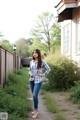 A woman in a plaid shirt and jeans standing on a path.