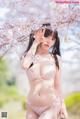 A woman in a white lingerie posing under a cherry blossom tree.