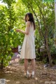 A woman in a white dress standing in the woods.