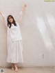 A woman standing in front of a white wall with her arms up.