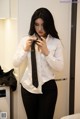 A woman in a white shirt and black pants adjusting a tie.