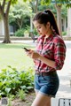 A woman in a plaid shirt and denim shorts looking at her phone.