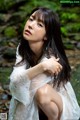 A woman in a white dress sitting on a rock in the woods.