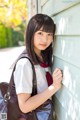 A young woman leaning against a wall with a brown bag.