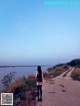 A woman walking down a dirt road next to a body of water.