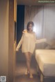 A woman in a white sweater is standing in a hotel room.