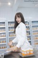 A woman in a white lab coat sitting at a counter in a pharmacy.